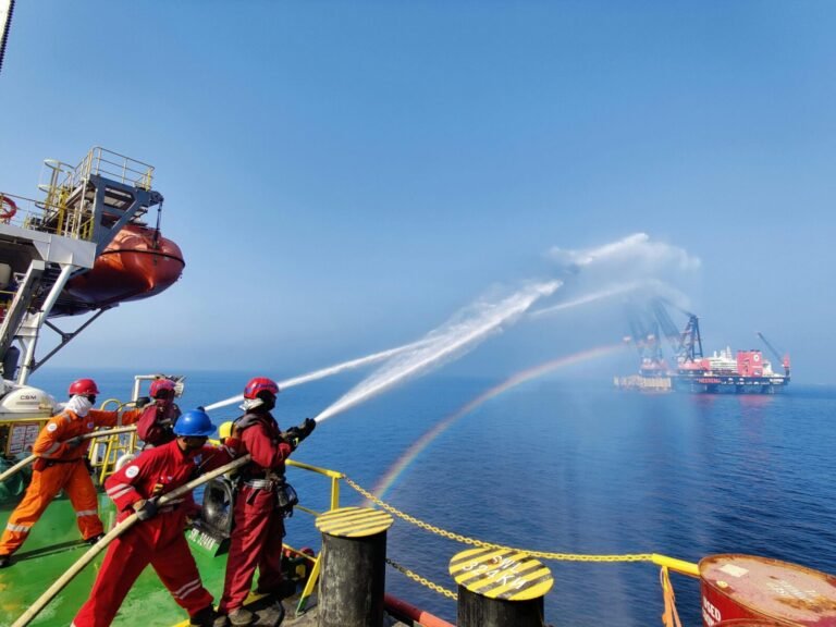 Workers on an offshore platform demonstrate teamwork using water hoses under a clear sky.